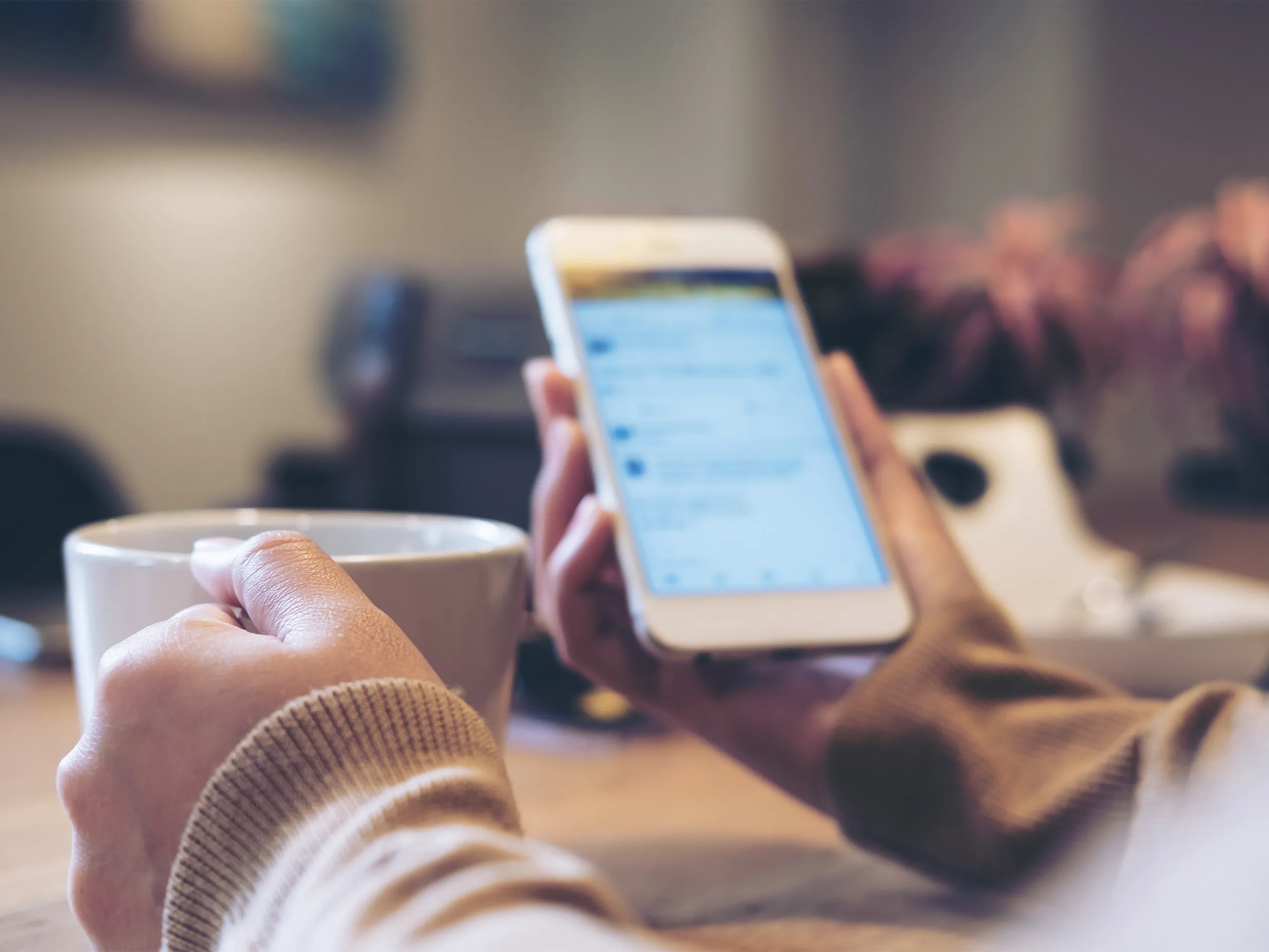 Person holding a cell phone and a mug