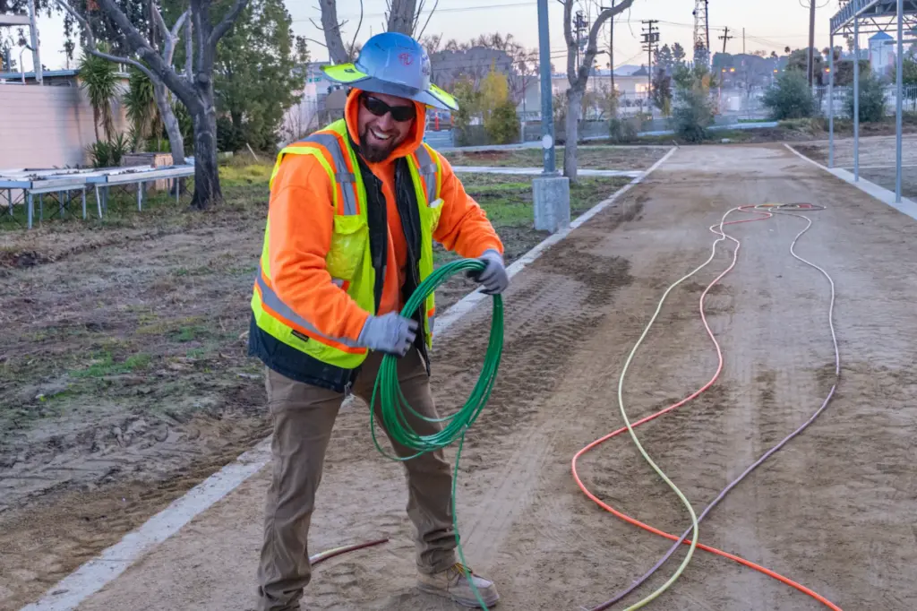 Man wearing safety gear holding coiled cables with dirt path background.
