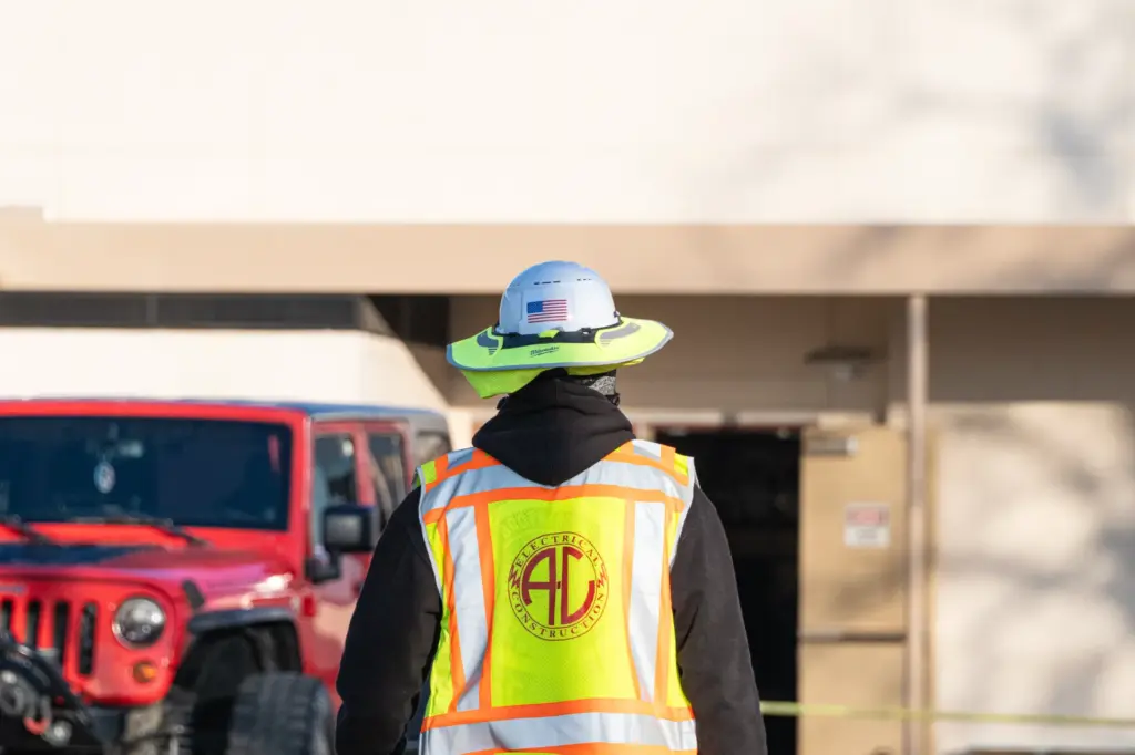A person wearing a reflective vest with logo is standing near cars and trucks at an industrial site.