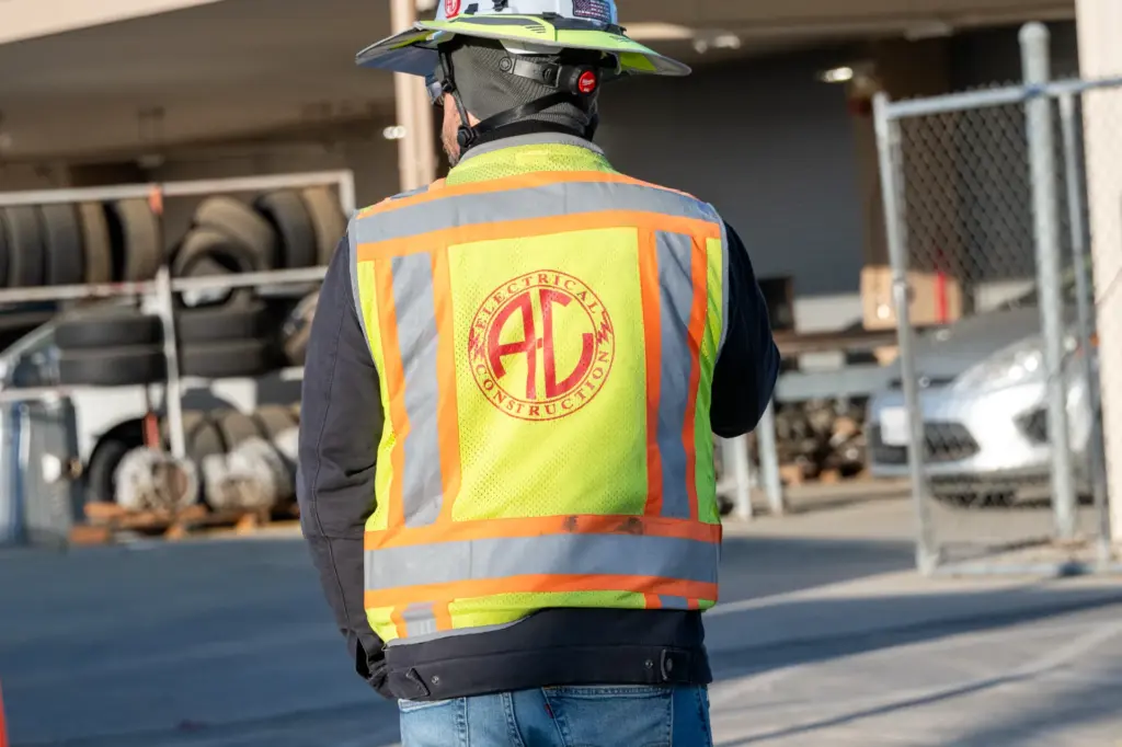 A person wearing a reflective vest with logo is standing near cars and trucks at an industrial site.
