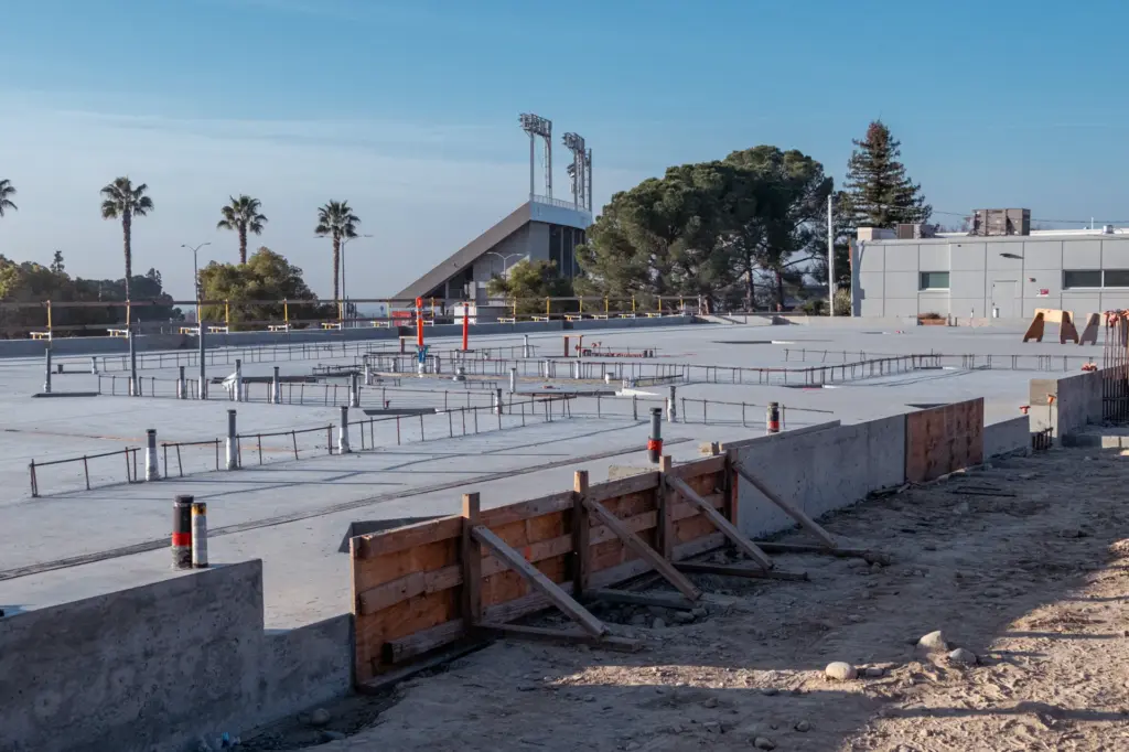 An outdoor construction site with buildings and trees in the background.