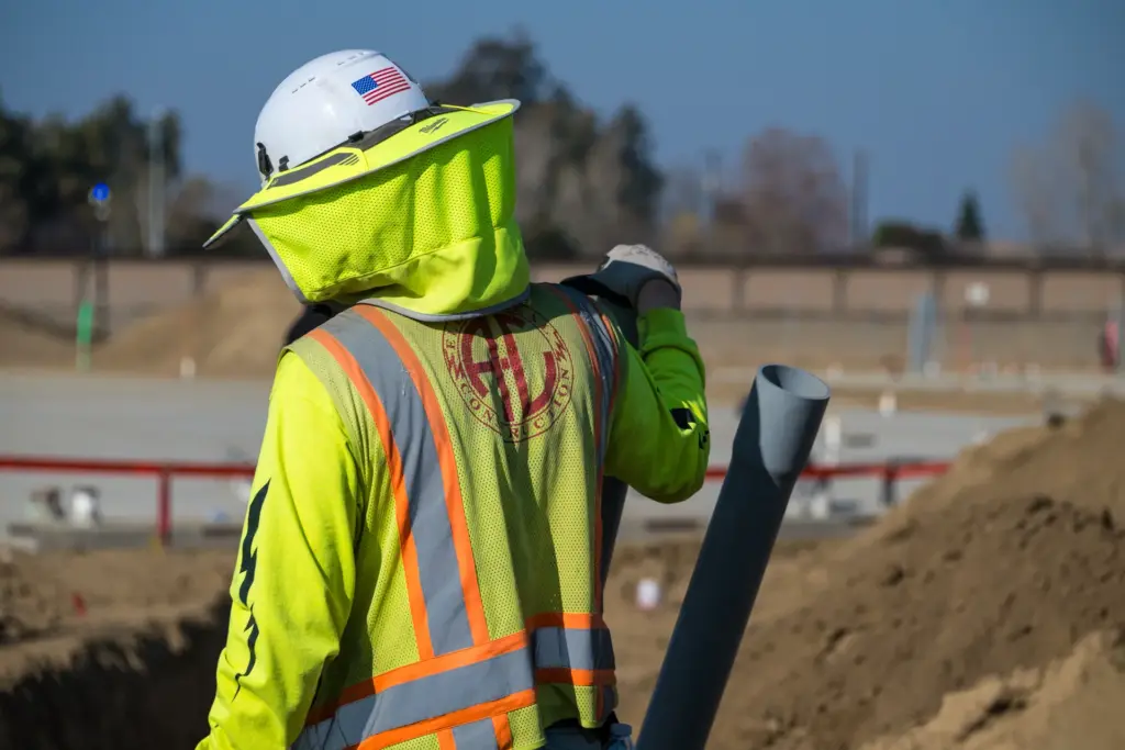 A construction worker is wearing a protective suit and holding an electrical conduit pipe.