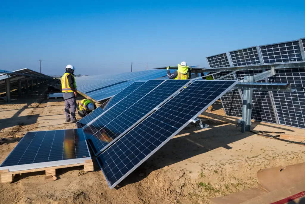 Two workers installing solar panels outdoors with a clear sky and blue background.
