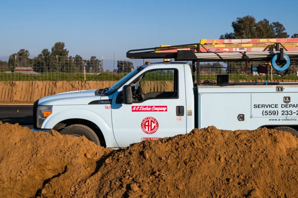 A blue truck with red and blue lettering drives is parked in front of a pile of dirt.