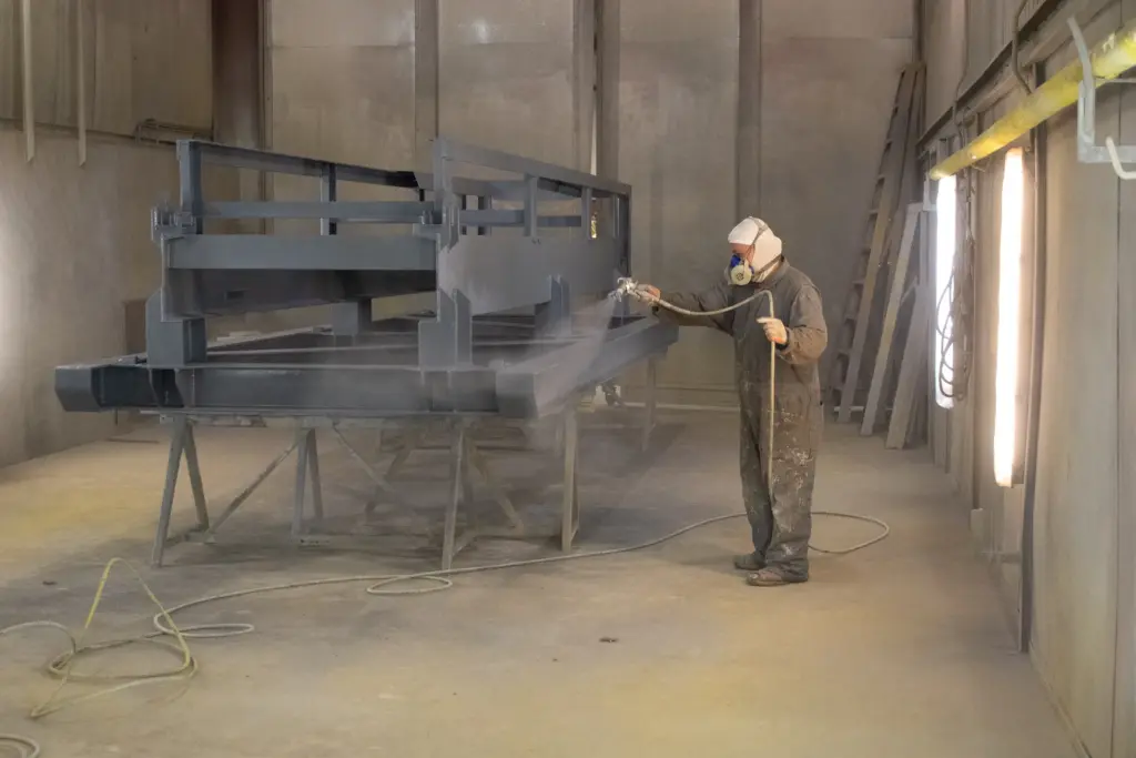 A person is spraying paint onto a metal structure with an air hose.