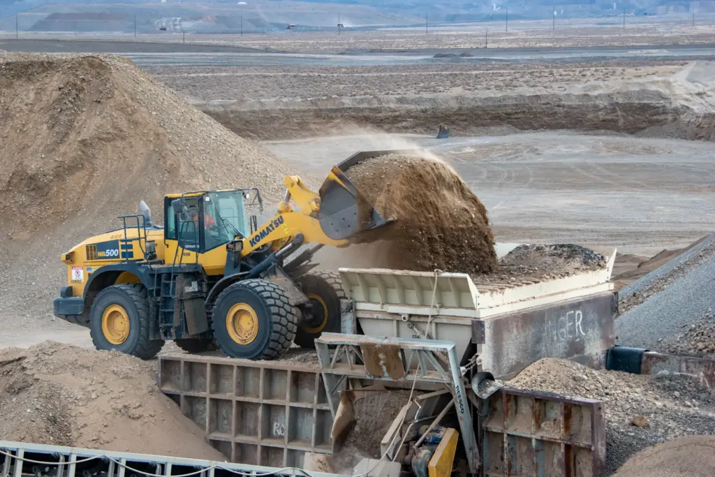 A yellow bulldozer is dumping sand into a feeder at an excavation site.