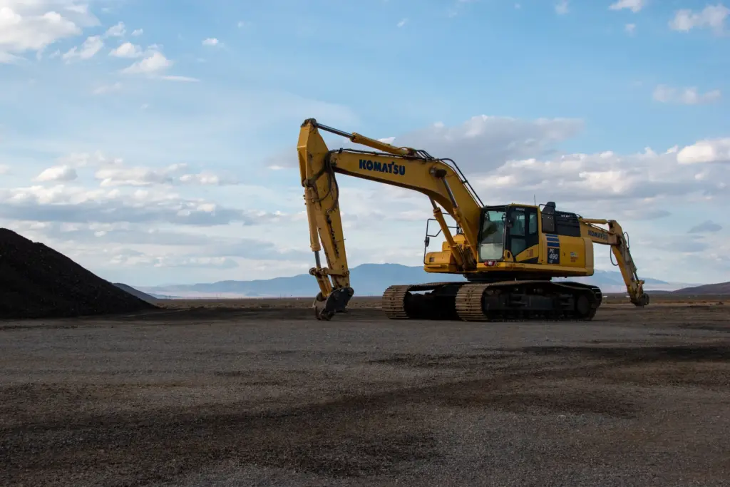 A yellow excavator is parked on a flat ground with mountains and sky in background.