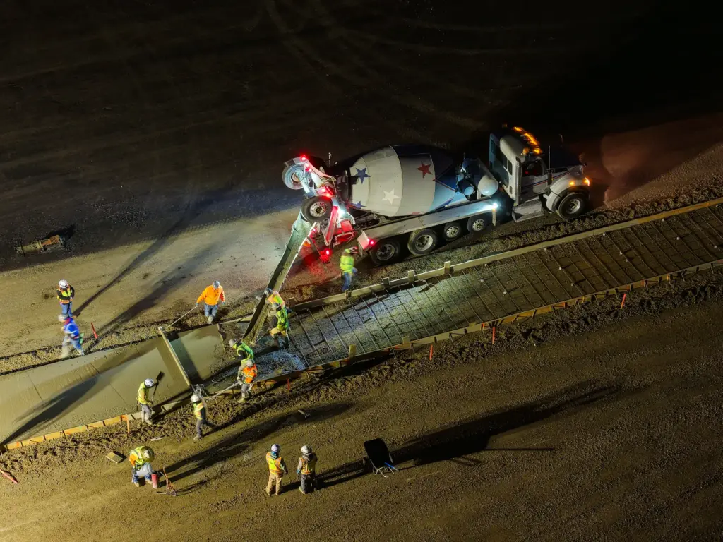 A construction crew is working at night with a concrete mixing truck on a concrete slab.