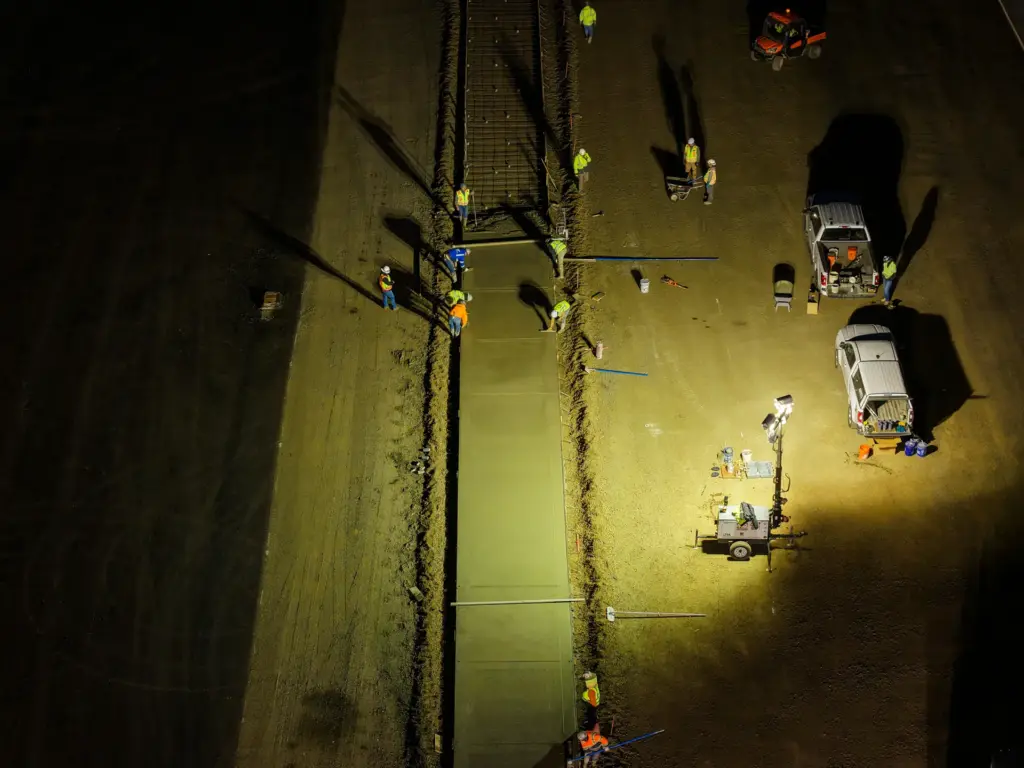 An aerial view of a concrete construction site at night with workers and vehicles.