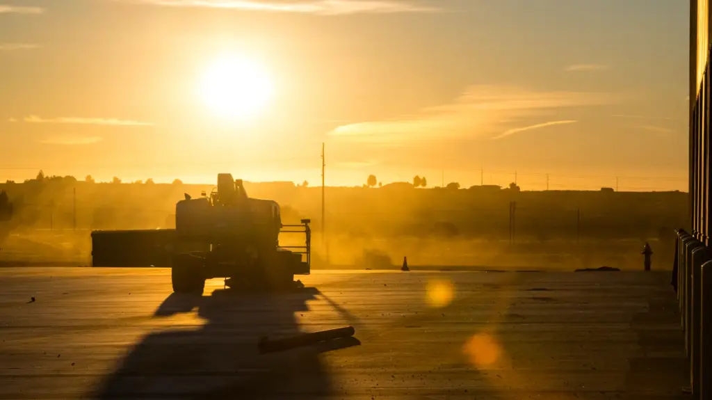 A truck is parked under a sunbeam at sunrise with buildings and dust particles in the air.