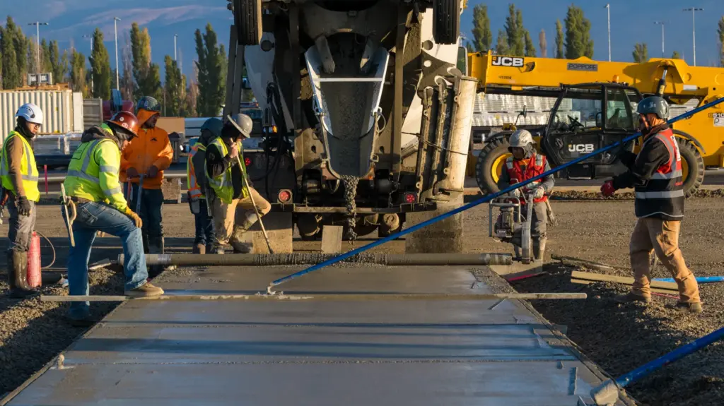 Workers around a concrete mixer truck at an industrial site.