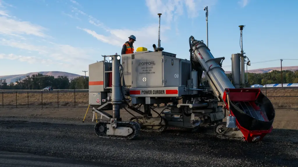 A curb machine construction vehicle with a person standing atop it.