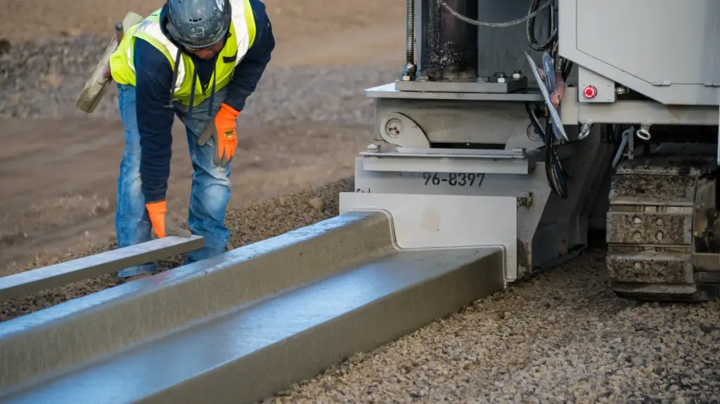 A construction worker is leveling out a concrete curb placed by a curb machine.