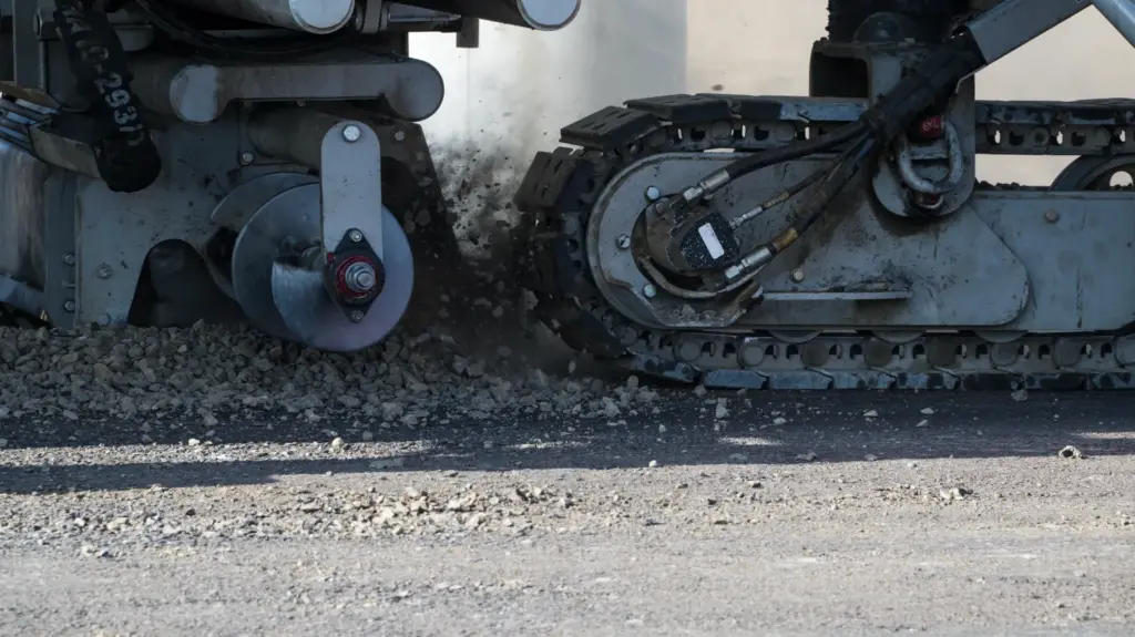 Close up view of a curbing machine kicking up asphalt aggregate.