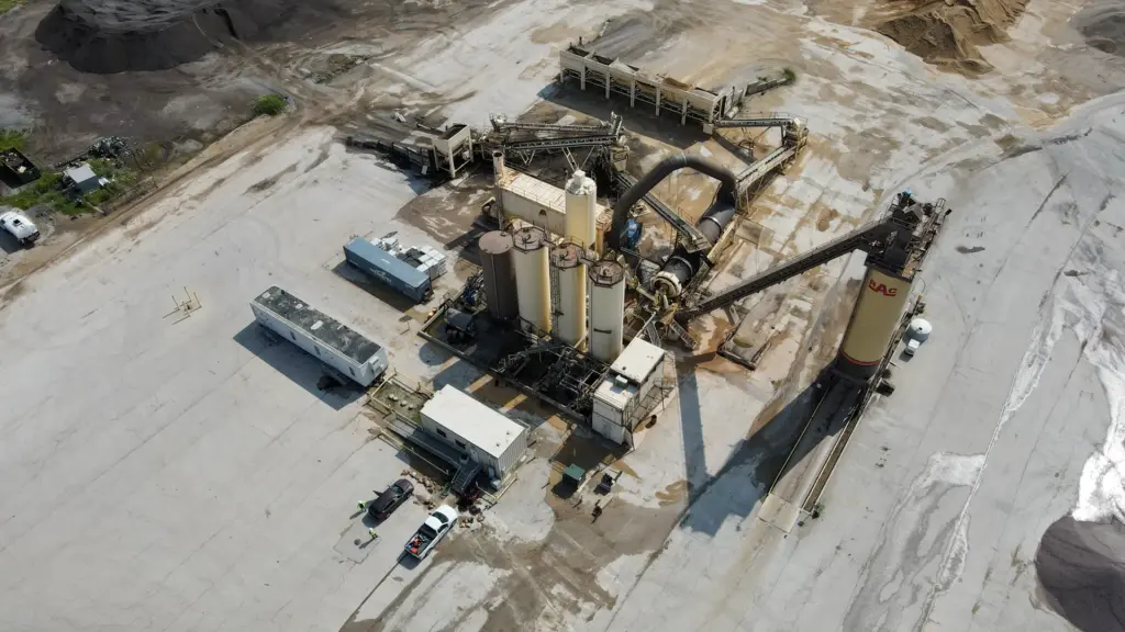 An aerial view of an asphalt plant site with machinery and vehicles surrounded by dirt.