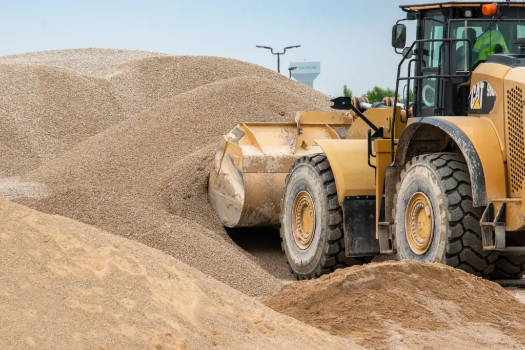 A yellow bulldozer is working with sand near a pile of it.