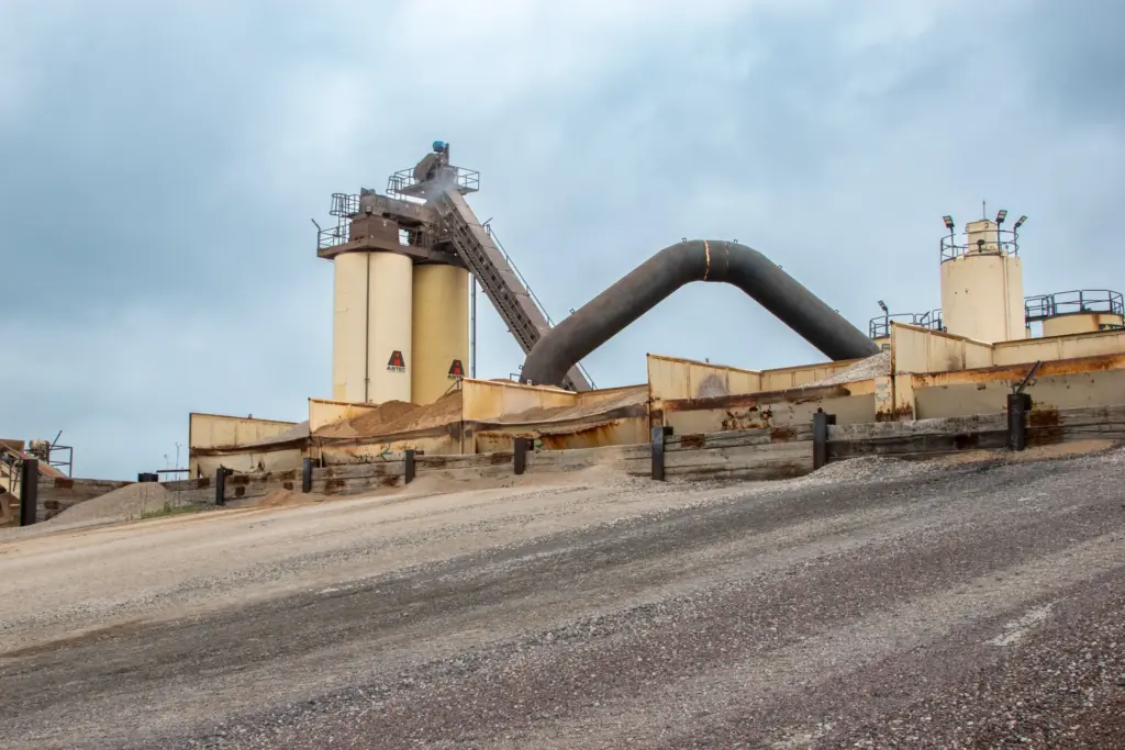 Asphalt plant with smoke and dust under a hazy sky.