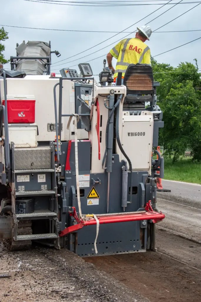 A person is working with a construction vehicle near trees and power lines.