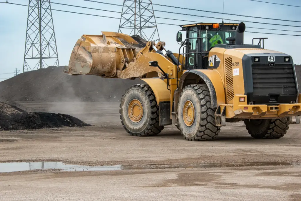 A yellow bulldozer is working at a construction site with power lines and dirt piles in the background.