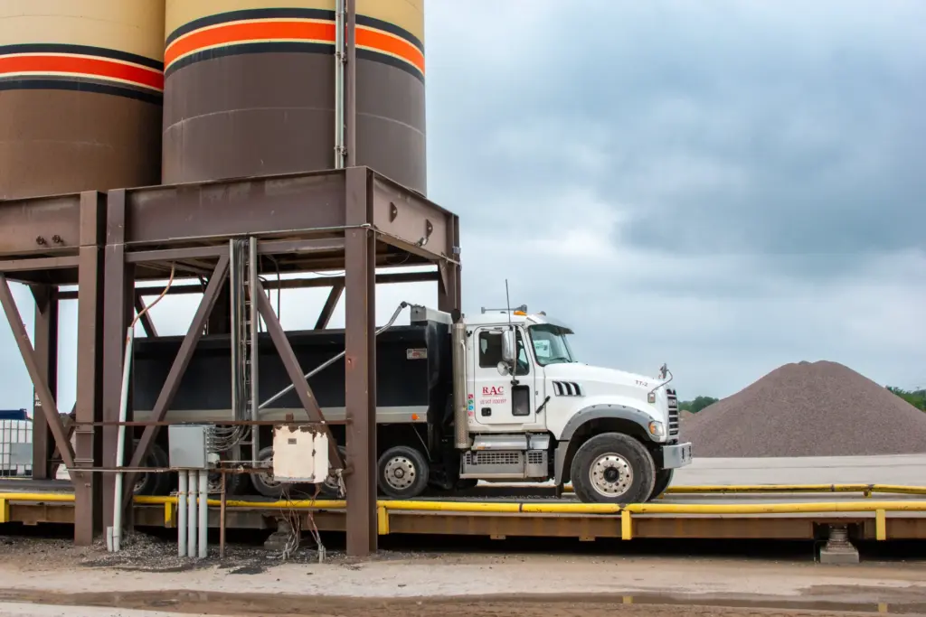 A loader truck is parked under two asphalt towers.