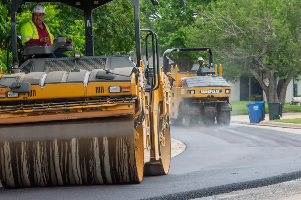 Two yellow road paving machines are driving down a street.