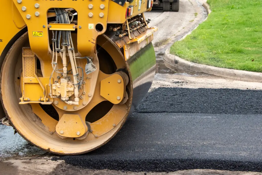 A yellow road roller is paving a street with asphalt.
