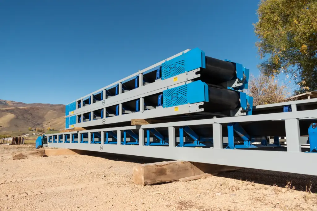 A stack of blue and gray aggregate conveyors outdoors with mountains in background.