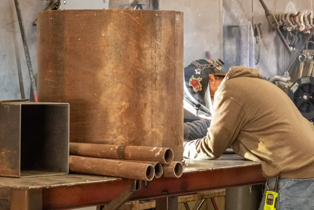 A person is welding a large brown object and tools at a workbench.