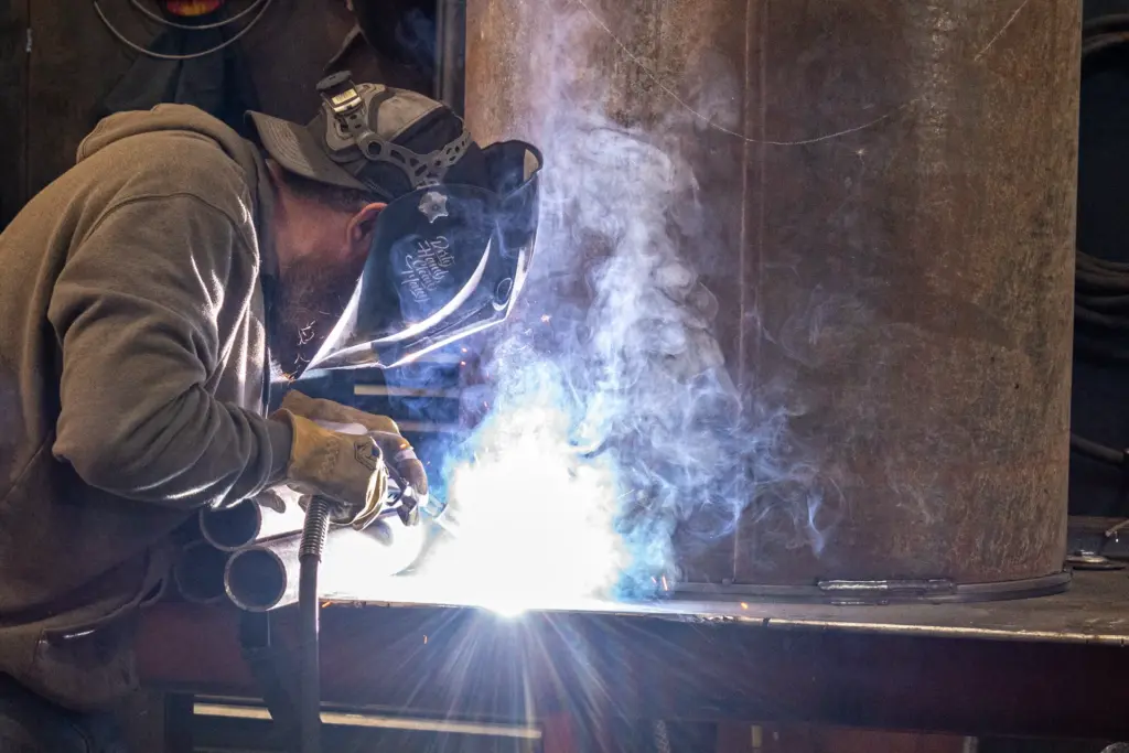 A person welding with smoke and light effects from a bright source behind them.