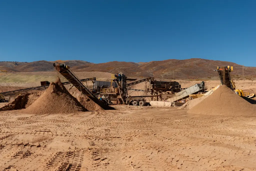 An aggregate quarry site with machinery and sand piles under a clear sky.